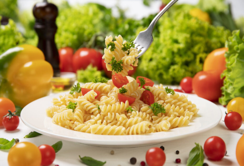 Plate of cooked italian fusilli pasta on fork with tomatoes and basil leaves